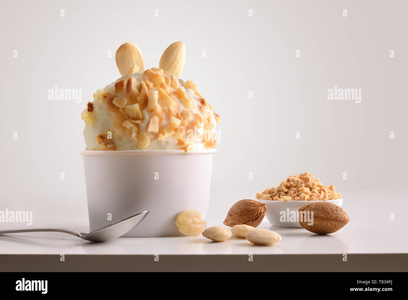 Zusammensetzung der Almond Ice Cream Ball in Pappbecher auf weißen Tisch mit Produkten von Ornament und Ausarbeitung isoliert Hintergrund. Horizontale Zusammensetzung Stockfoto