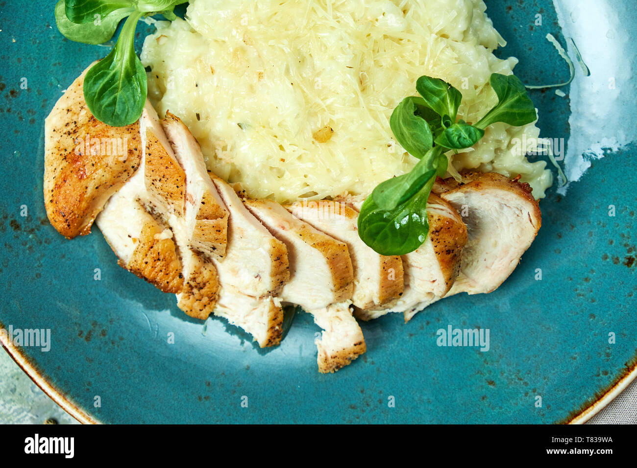 Weißer Reis mit Huhn Brust mit grünen auf einem blauen Schild. Rizotto. Graues Licht strukturierten Hintergrund mit Grau und Beige Stoff. Schöne Servieren von Speisen. Restaurant Menü Stockfoto