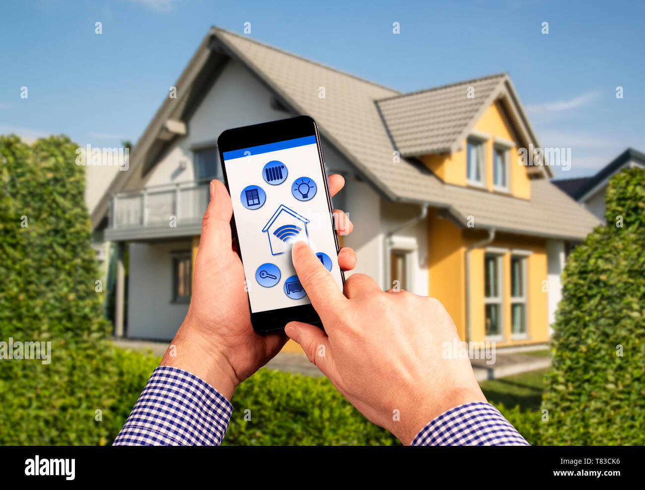 Eine Fernbedienung mit Symbolen für den Betrieb eines Smart Home mit Haus im Hintergrund Stockfoto