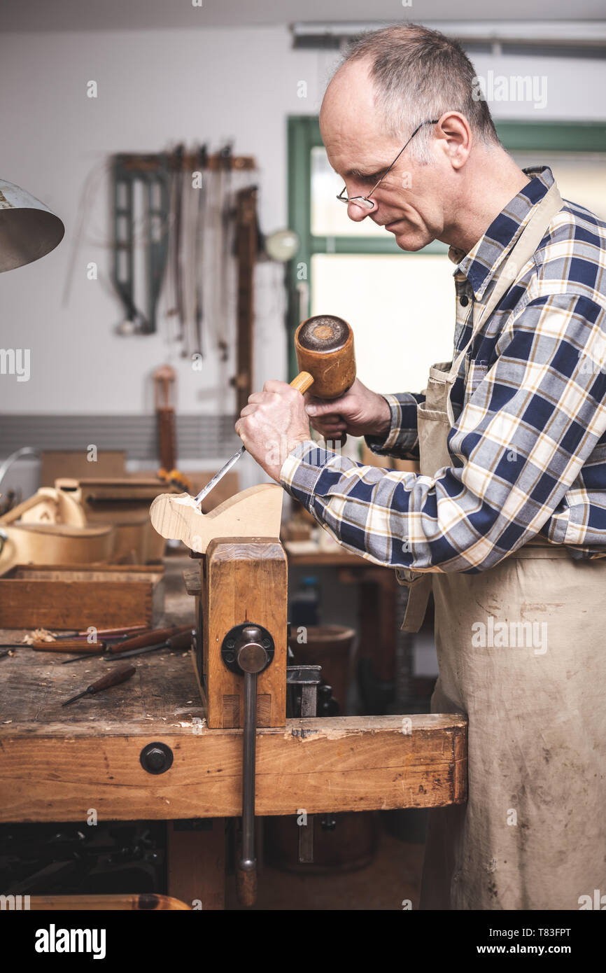 Erfahrene Handwerker konzentrierte sich auf das Schnitzen eines Holzfigur mit Meißel und Hammer Stockfoto