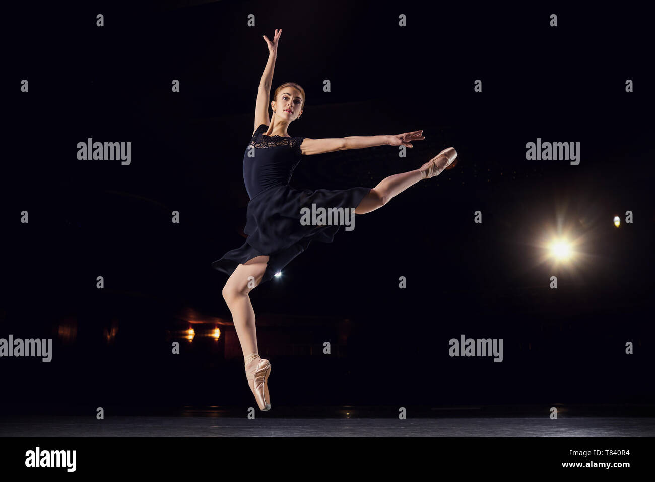Ballerina in einen schwarzen Anzug ist das Springen auf einem schwarzen Hintergrund. Stockfoto