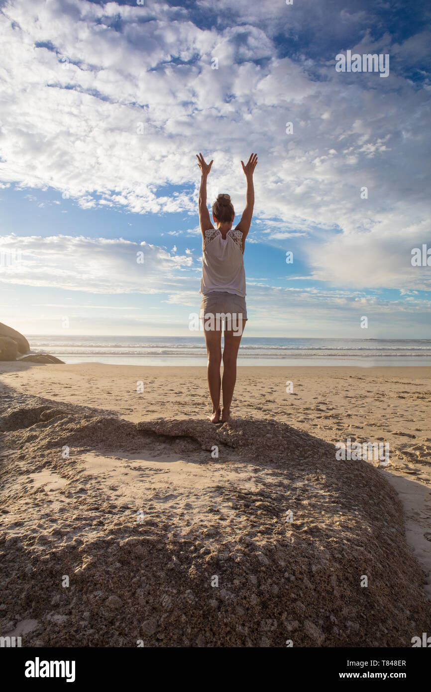 Frau am Strand mit erhobenen Händen üben Yoga, Rückansicht, Cape Town, Western Cape, Südafrika Stockfoto