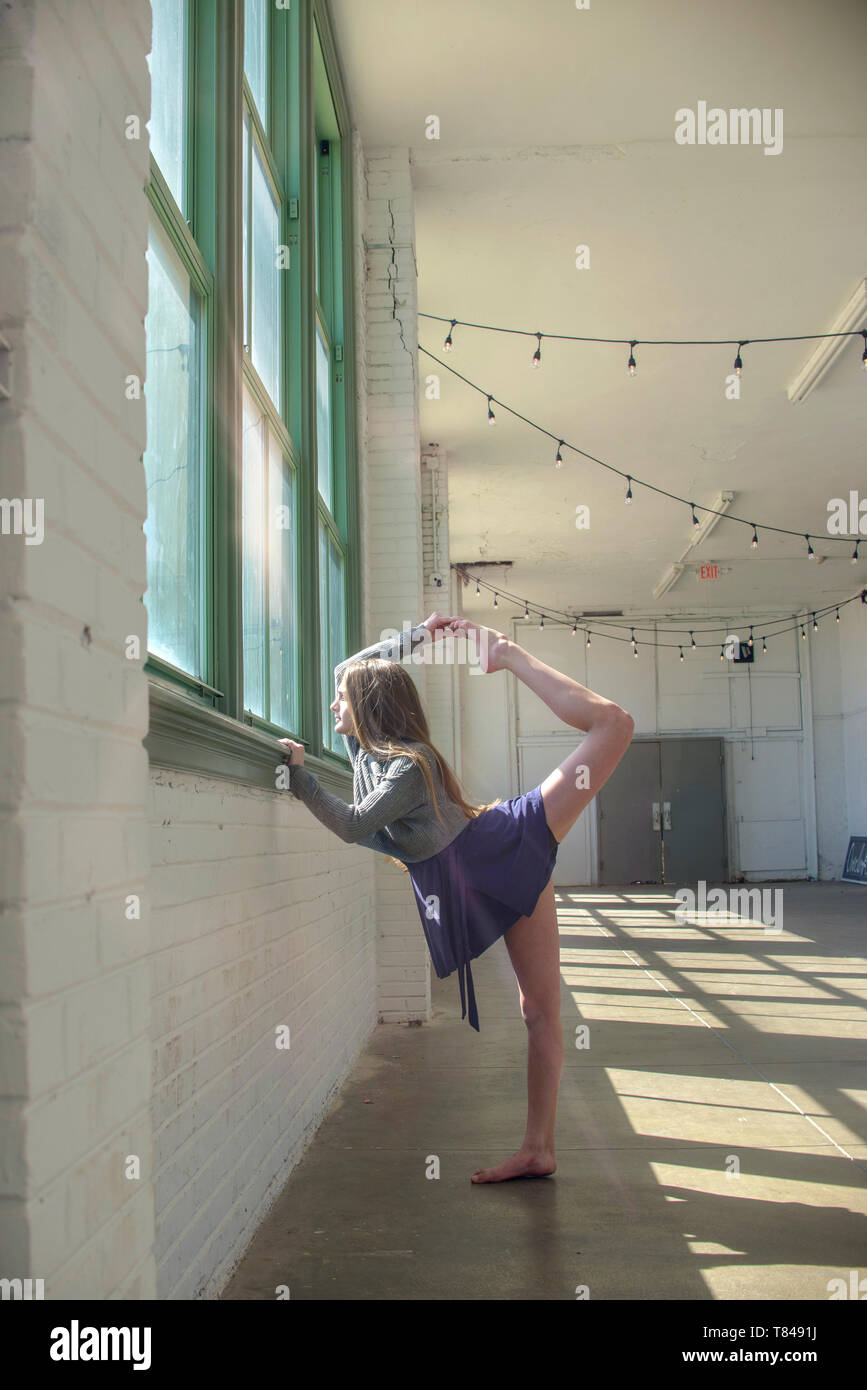 Junges Mädchen suchen durch Tanz Studio Fenster balanciert, Holding angehoben Bein Stockfoto