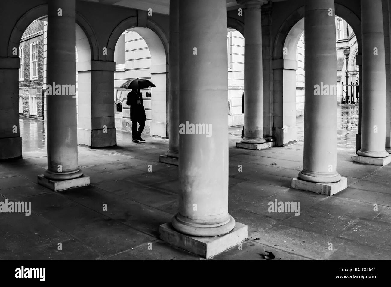 Tempel, London, Großbritannien - 8. Februar 2019 - ein Mann mit umbralla Spaziergänge durch collonnade an einem windigen Tag Stockfoto