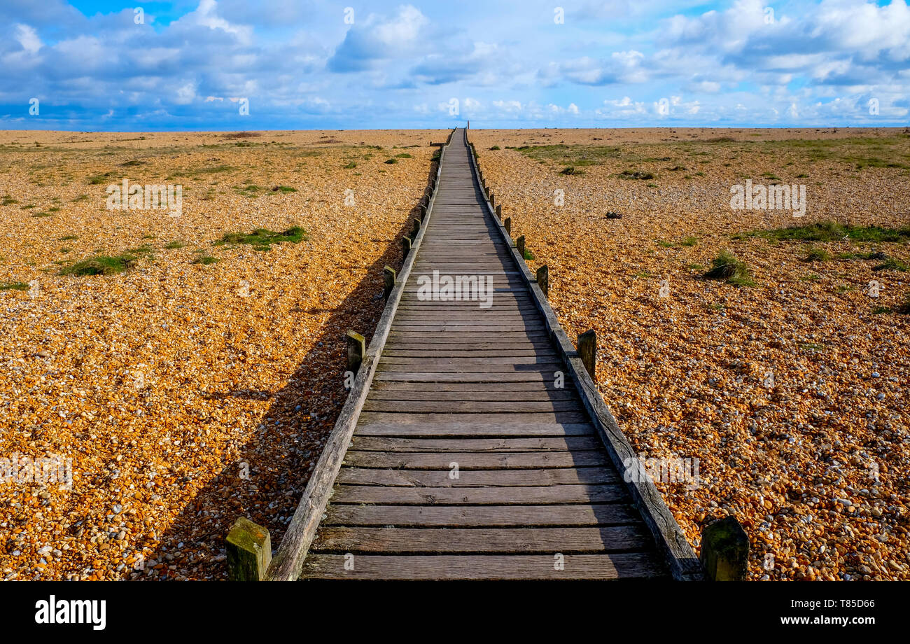 Eine lange Gerade Holzterrasse weg mit einem diminshing Perspektive auf einen Kiesstrand, der Weg große im Vordergrund Zentrum des Bildes beginnt Stockfoto