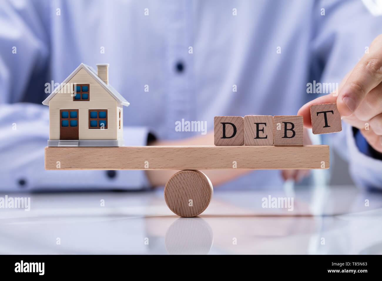 Nahaufnahme der Geschäftsmann Hand Wort Schuld auf Holz- Wippe zum Ausgleich Modell Haus Stockfoto