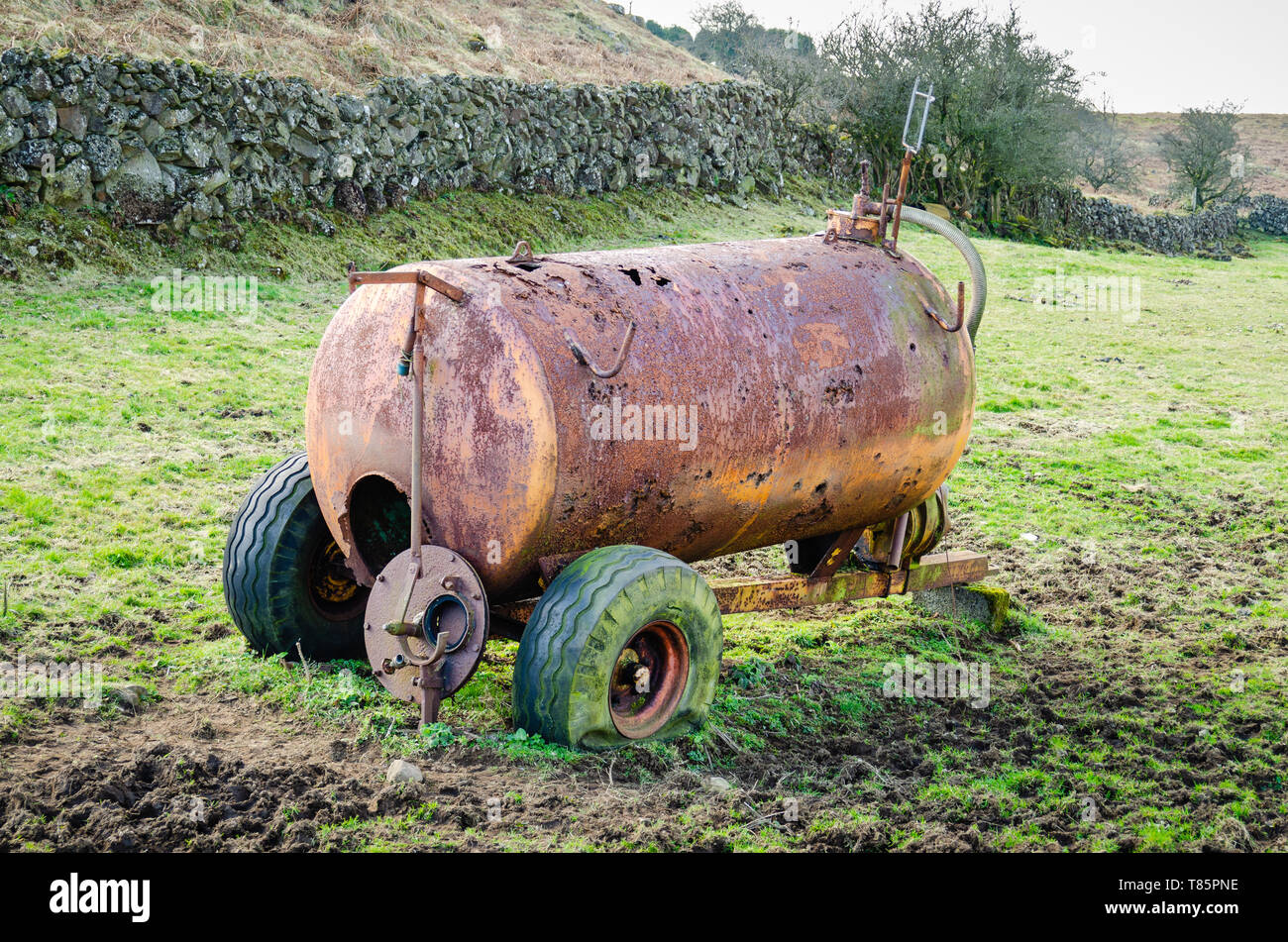 Eine rostige, korrodierte slurry Tanker mit platten Reifen sitzt in ein schlammiges Feld in der irischen Landschaft aufgegeben. Stockfoto