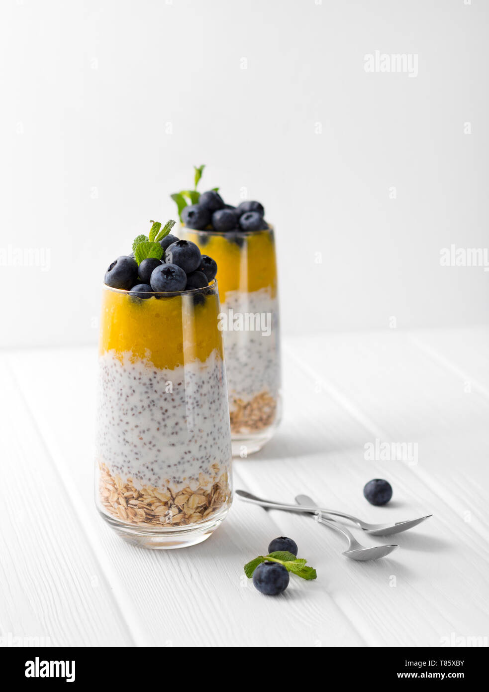 Glas Joghurt mit Chia Samen, Blaubeeren und Mango Mousse und Haferflocken auf einem weißen Holztisch. Stockfoto