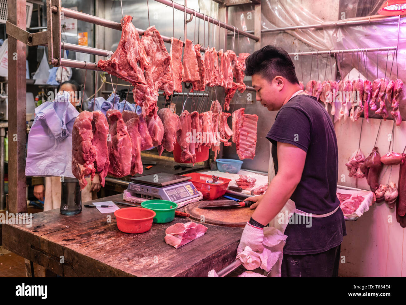 Hong Kong, China - 8. März 2019: Tai Po Markt in Neuland. Breitere Schuß von jungen Metzger schneidet Stücke von rotem Fleisch auf seinem dicken Holz Werkbank. Stockfoto