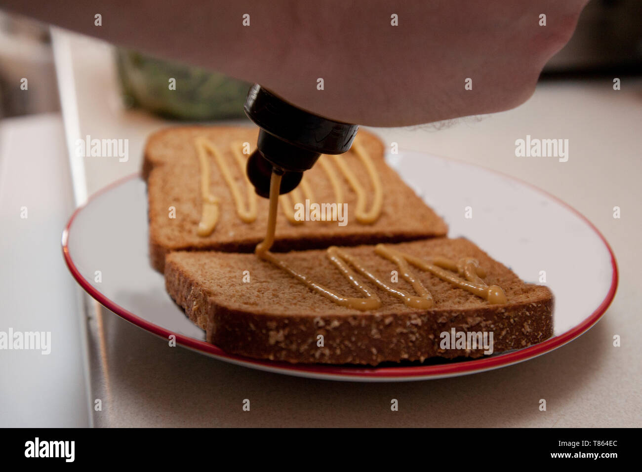 Eine Person ist Gießen Senf auf ihr Brot ein Sandwich zu machen Stockfoto