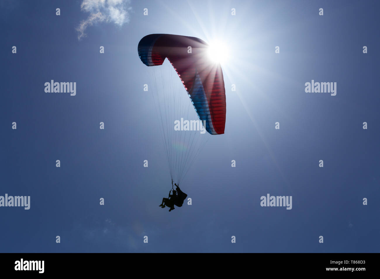 Eine Silhouette von Tandem Gleitschirme mit rote Rutsche fliegen, die in der gesamten Sun Stockfoto