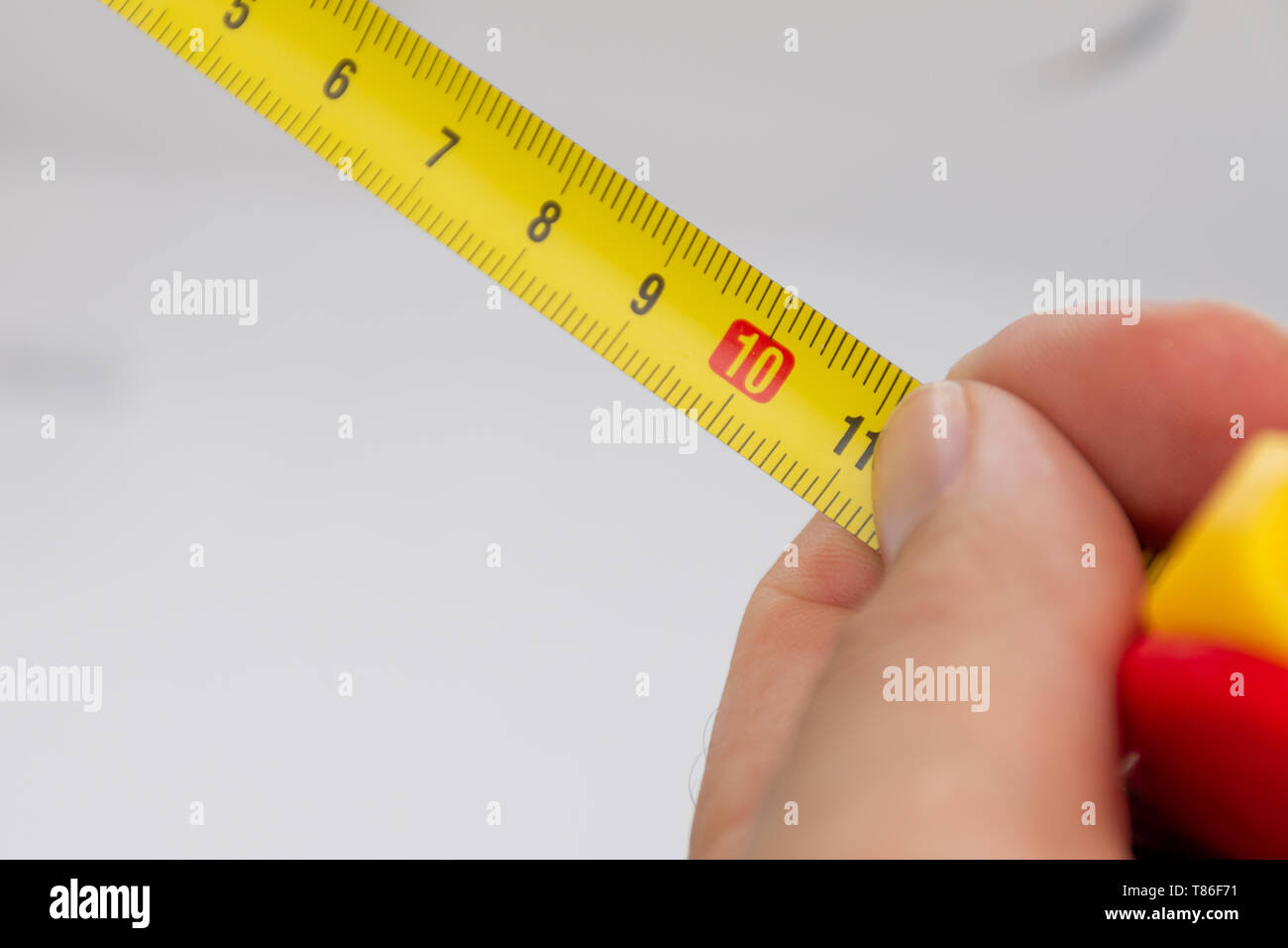 Eine Nahaufnahme von einem gelben metrischen Maßband mit einer weißen Hand schließen für Präzision. Stockfoto