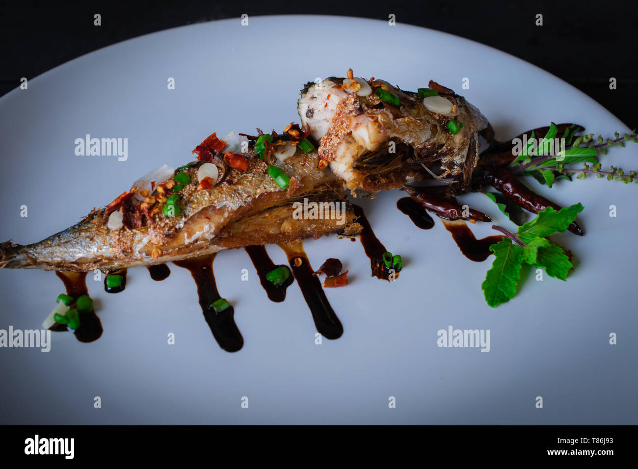 Saba gebratener Fisch mit Sauce auf weiße Platte und Dekoration von Gemüse und Soße auf den Tisch. Stockfoto