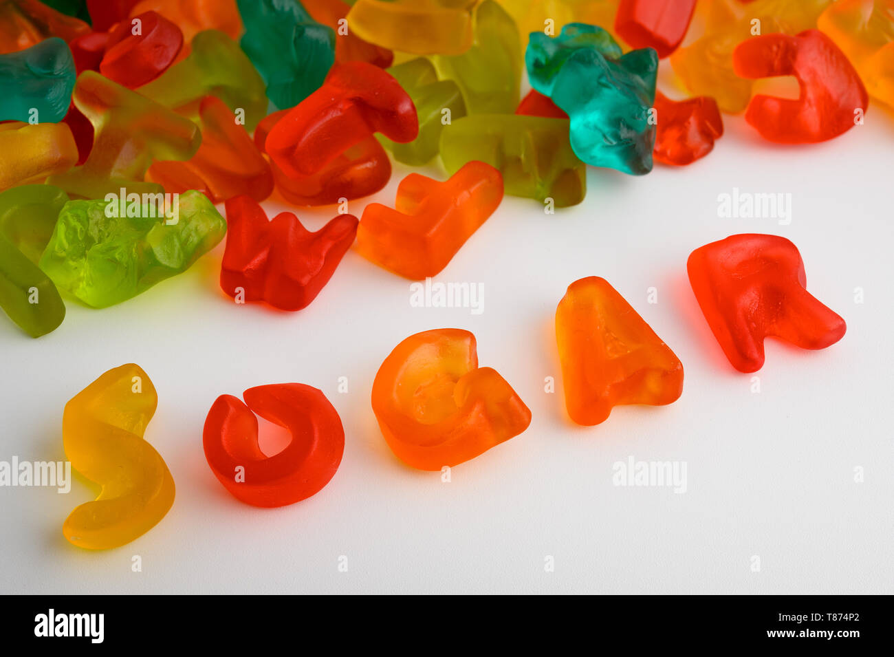Bunte Gummibärchen Bonbons auf weißem Hintergrund mit dem Wort Zucker mit Süßigkeiten geschrieben Stockfoto
