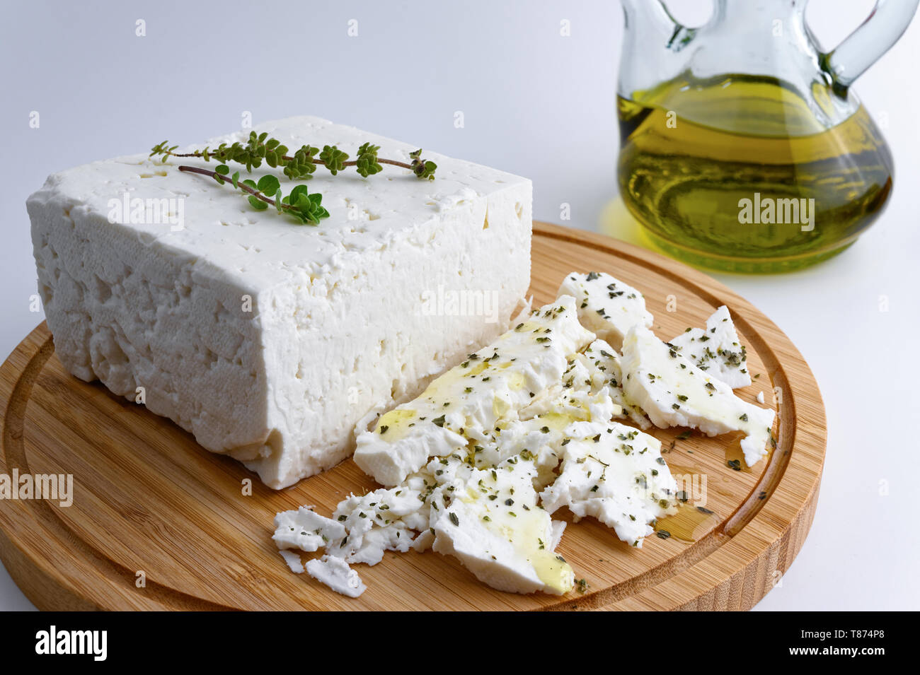 Großes Stück traditioneller griechischer Schafskäse auf Holz Schneidebrett mit Oregano und nativem Olivenöl extra auf weißem Hintergrund Stockfoto