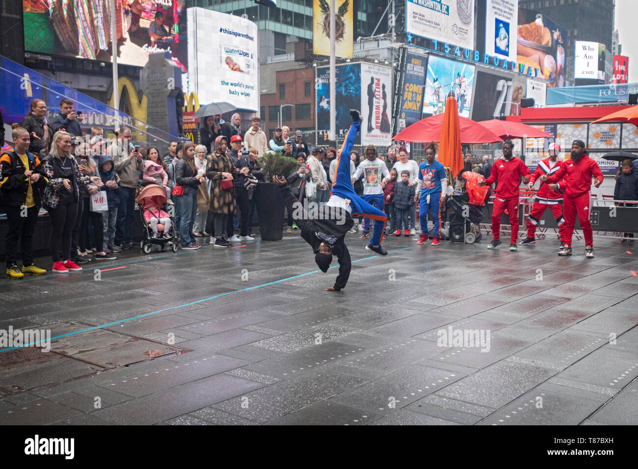 Acrobat Gymnastik Gaukler durchführen für eine Masse von Touristen an einem regnerischen Wochenende Morgen. Times Square, Manhattan, New York City. Stockfoto