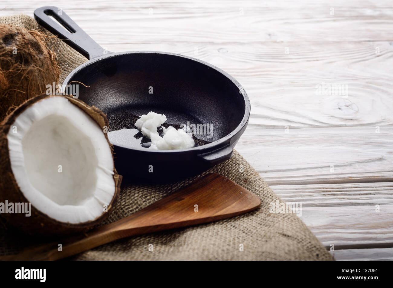 Kokosnuss, Shell mit Fleisch, Gusseisen Skillet und Spachtel auf Hanf Sack auf weißen Küche aus Holz Tisch Stockfoto