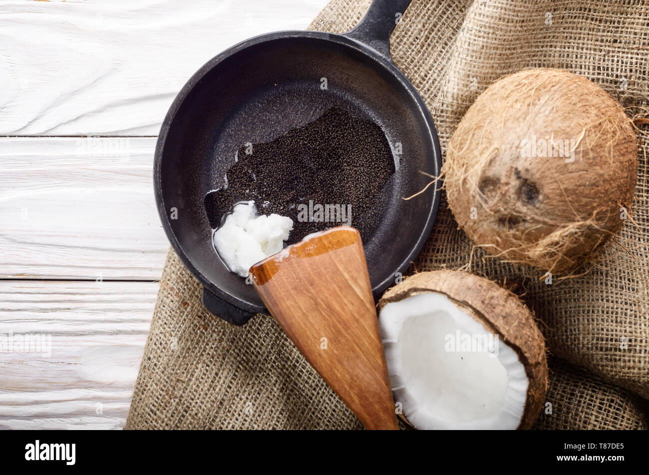 Kokosnuss, Shell mit Fleisch, Gusseisen Skillet und Spachtel auf Hanf Sack auf weißen Küche aus Holz Tisch Stockfoto