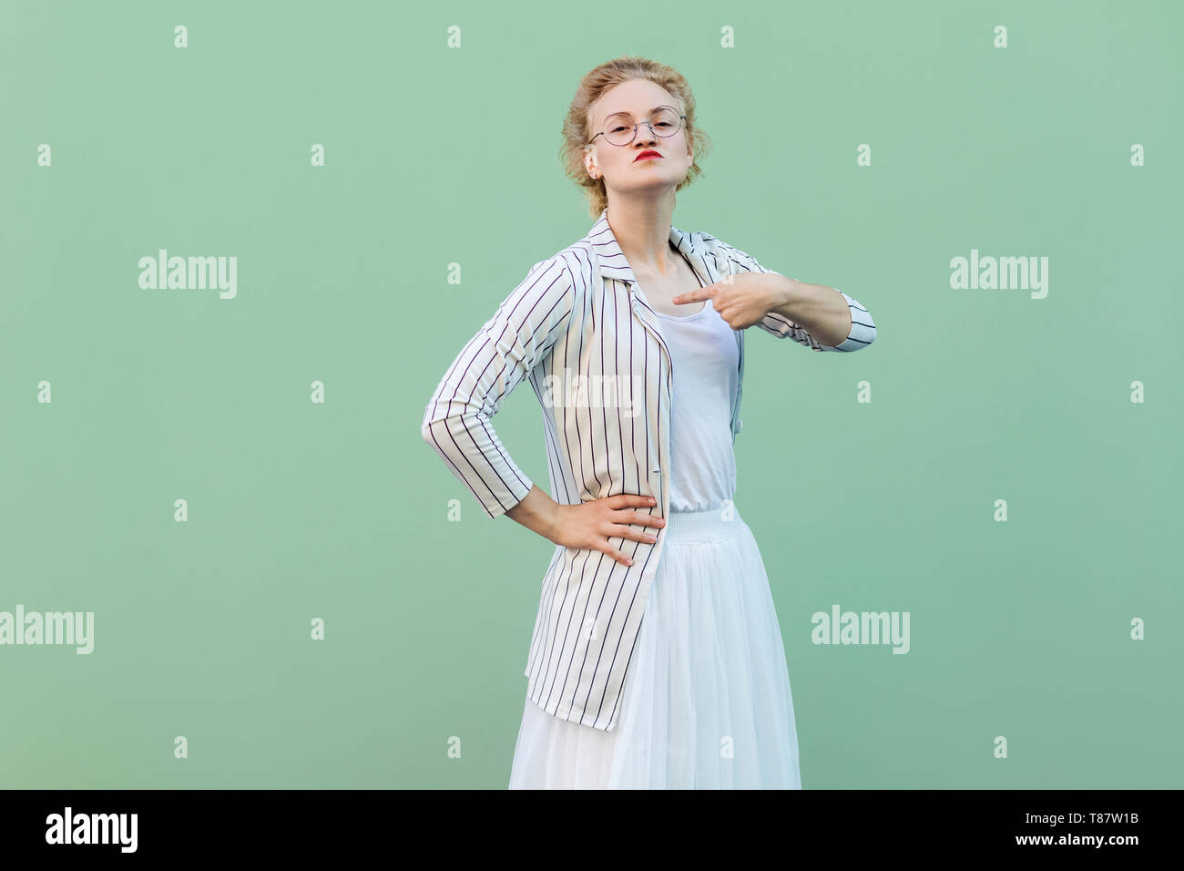 Das bin ich! Portrait von Stolz, junge Frau in weiß gestreifte Bluse mit Brille stehen mit Hand auf Taille, sich zeigen und auf Kamera. Stockfoto