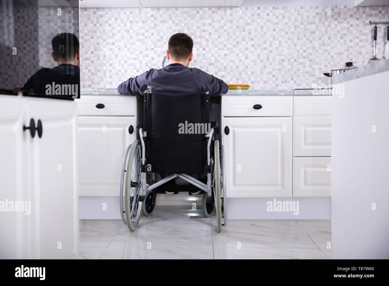Behinderte Mann sitzt auf Rollstuhl Waschen und Reinigung Geschirr in der Küche Stockfoto
