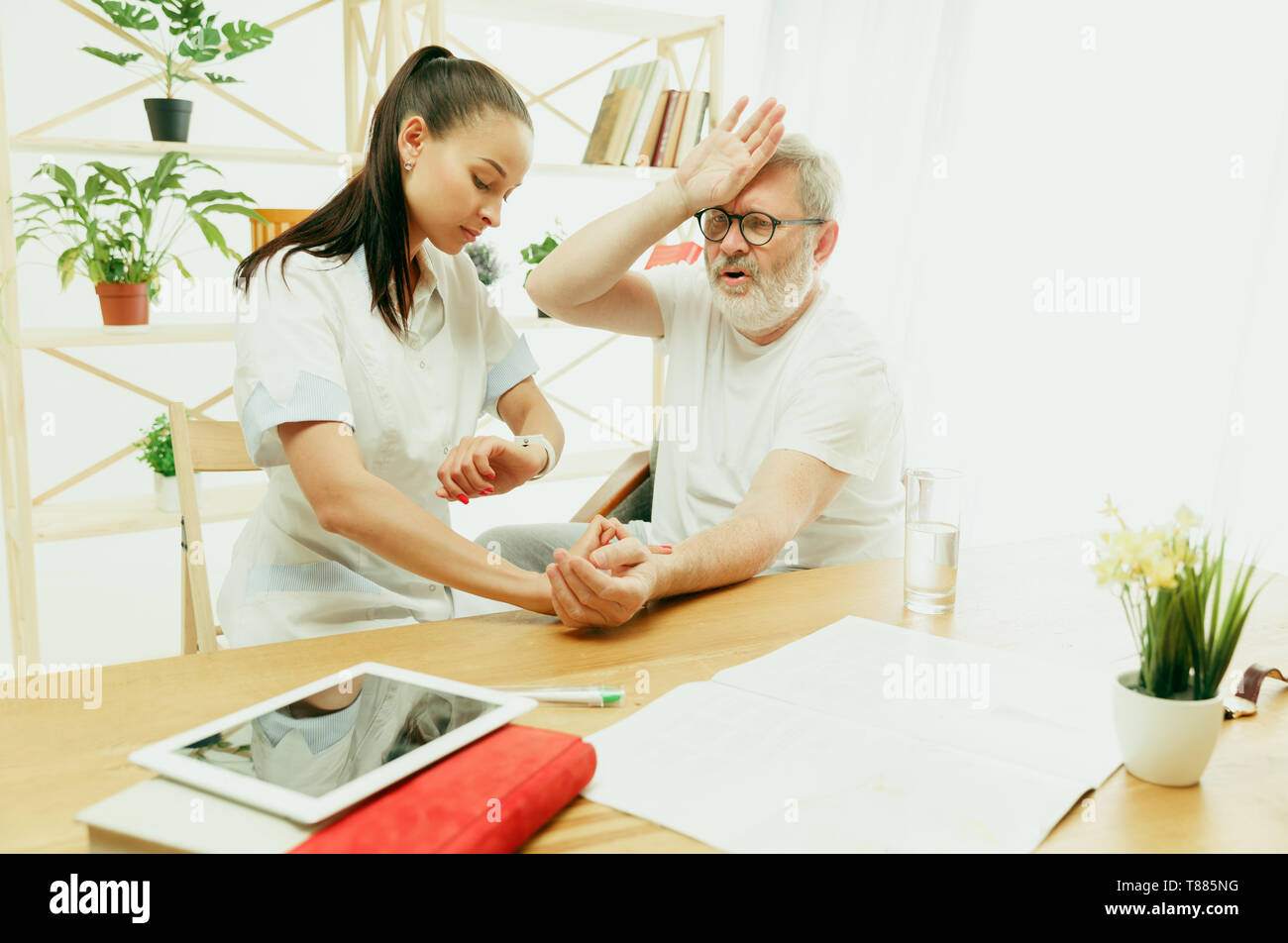 Der Besuch einer Krankenschwester oder Gesundheit Besucher die Pflege von älteren Menschen. Lifestyle Portrait zu Hause. Medizin, Gesundheit und Prävention. Mädchen der Kontrolle oder Messung der Puls des Patienten während des Besuchs. Stockfoto