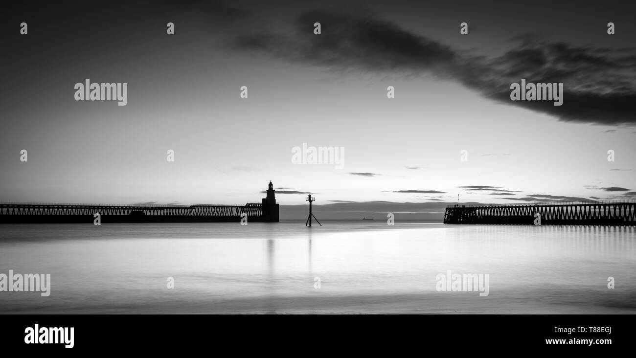 Frühen kalten Wintermorgen die orange Sunrise, die Silhouetten der Blyth port Piers & Hafen Leuchtturm in Northumberland zu fangen Stockfoto