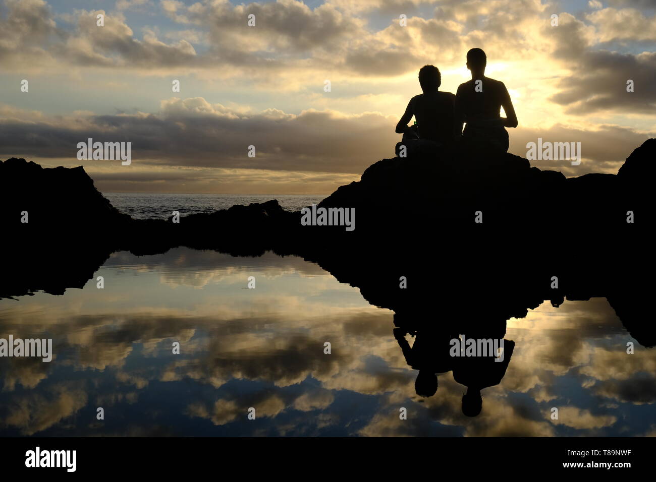 Von hinten mit Licht schoss auf dem Hintergrund von zwei Menschen den Sonnenuntergang mit Reflexionen auf dem Wasser Stockfoto