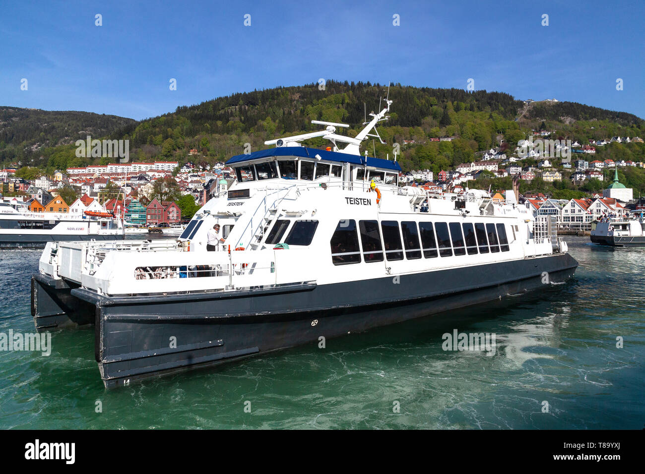 Lokale Fahrgast Katamaran Teisten aus Strandkaien Anschlußklemme n Hafen von Bergen, Norwegen abfliegen. Hanseatic Bryggen im Hintergrund. Stockfoto