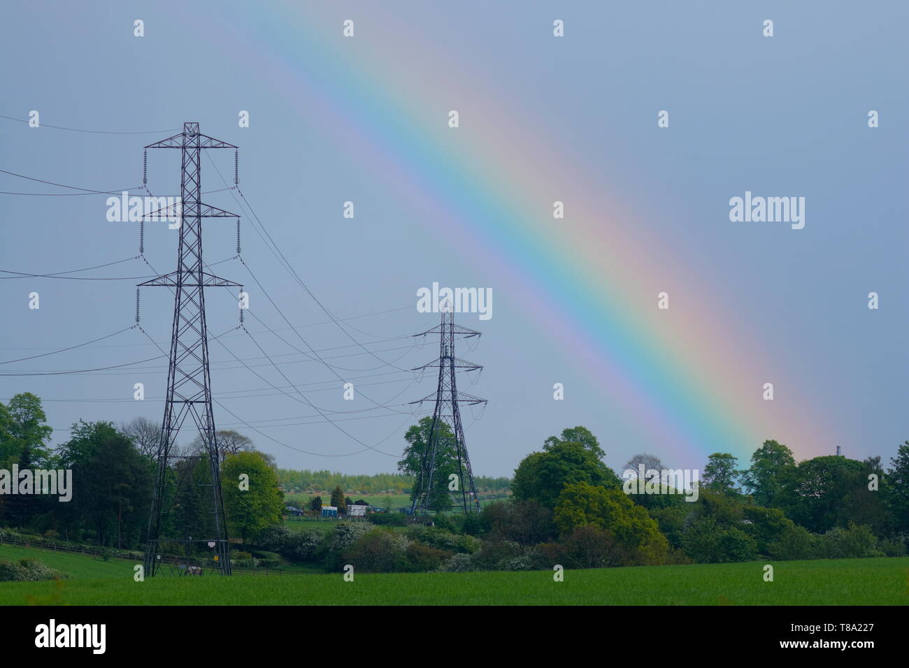 Pylone, die mit einem Regenbogen durch die ländliche Landschaft führen Stockfoto