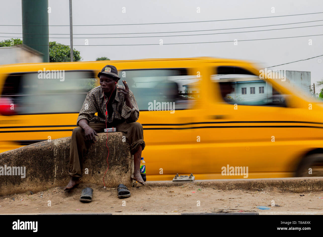 Ein Obdachloser sitzt und raucht inmitten einer Autobahn in Lagos, Nigeria. Stockfoto