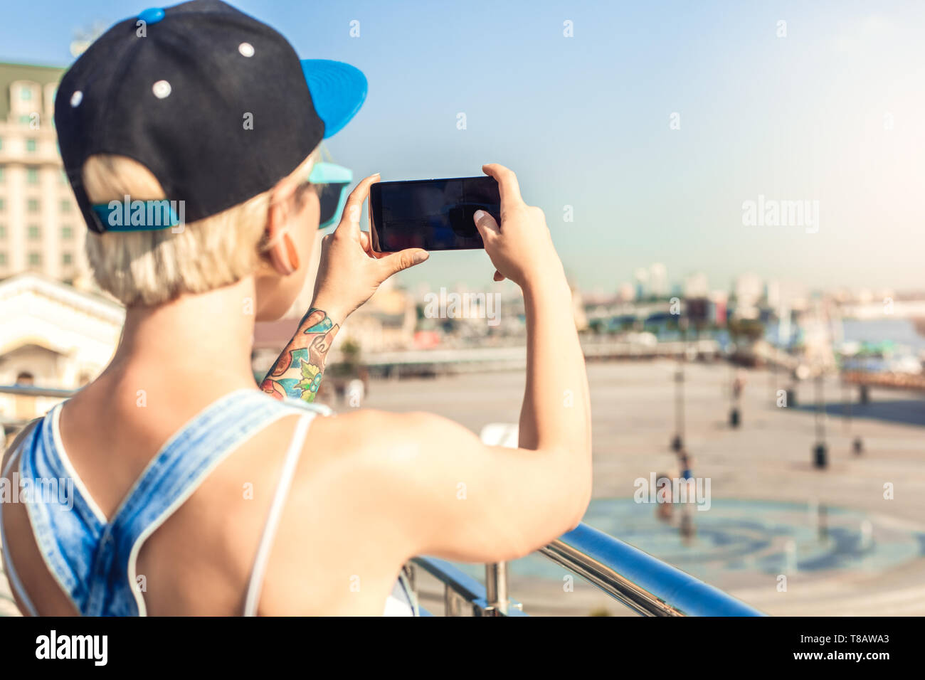 Sommer. Alternative Mädchen in der Kappe und Sonnenbrille auf der Straße der Stadt, Foto auf dem Smartphone close-up Stockfoto