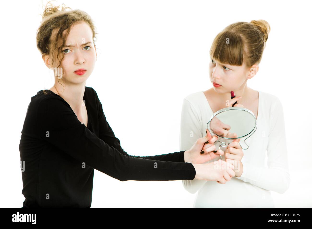 Zwei der Pubertät Mädchen in schwarzen und weißen Kleider Feilschen einen Spiegel zu einem Make-up Make-Schwester Rivalität - weißer Hintergrund zu erhalten Stockfoto