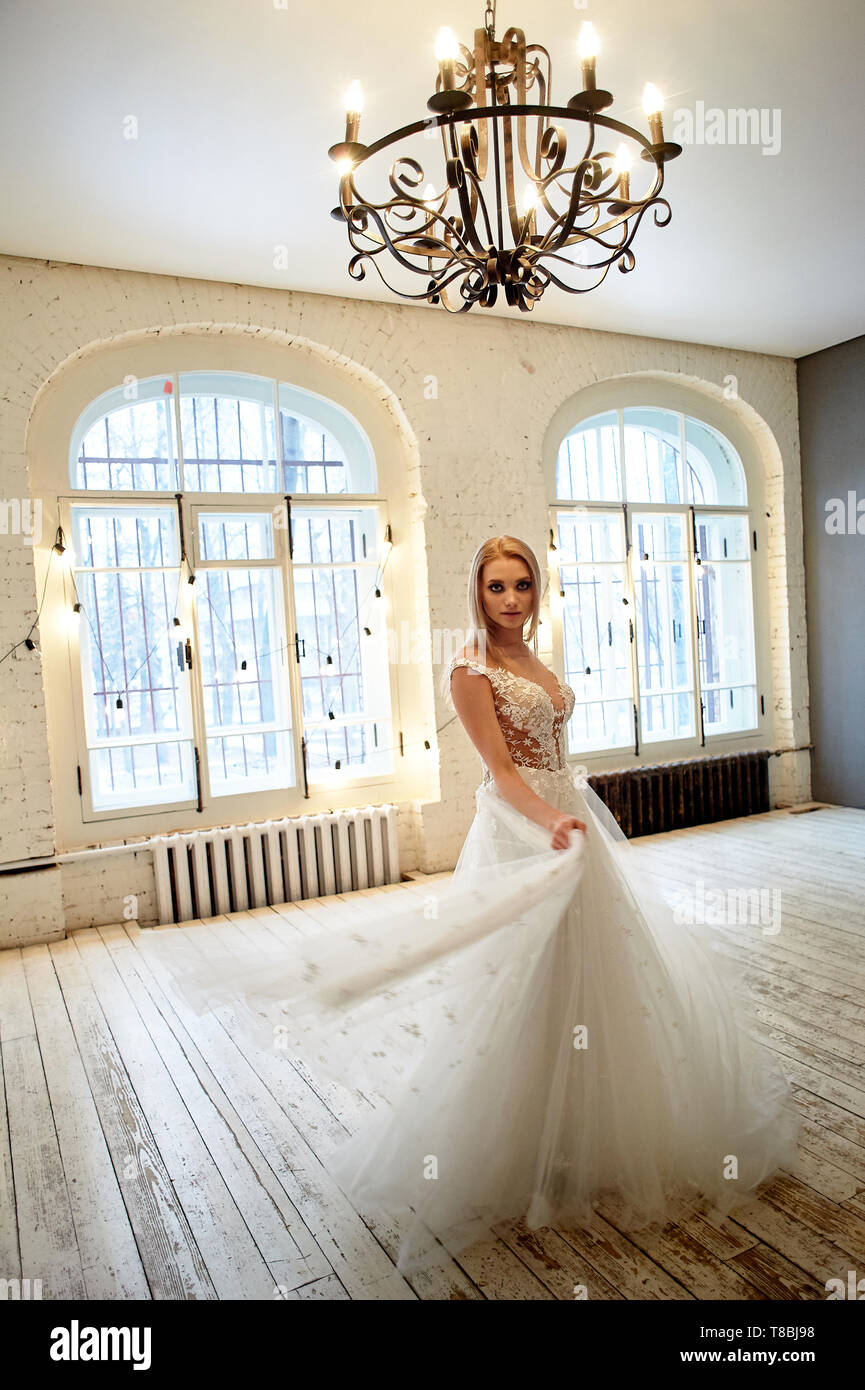 Die Braut in einem weißen Kleid mit besticktem Oberteil ist die Spinnerei im Loft-stil Zimmer. High Key. Stockfoto