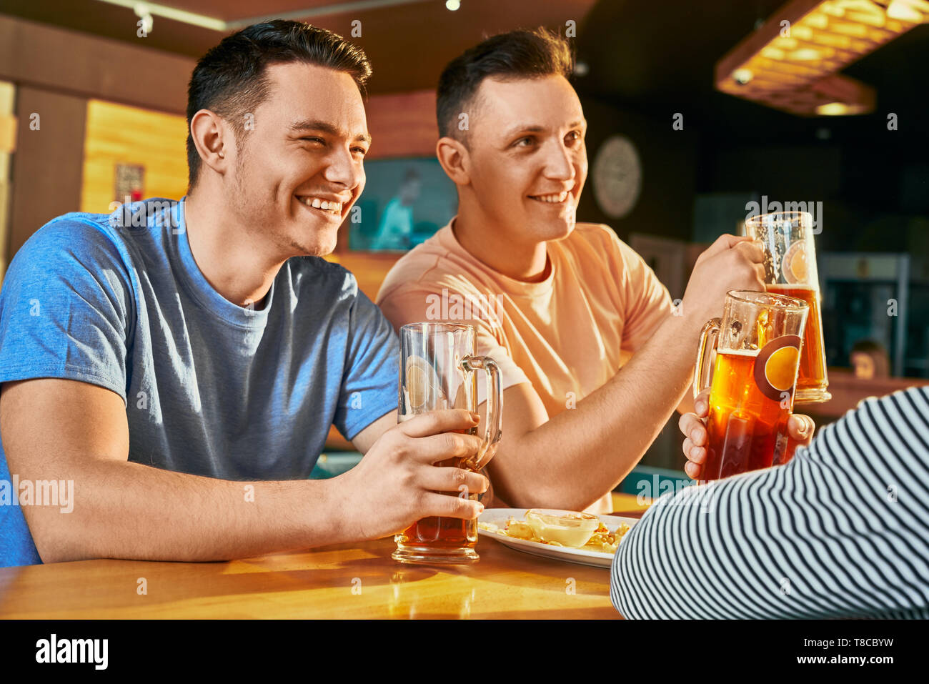 Ansicht von der Seite der zwei glückliche Männer ruht mit Freunden in der Bar, trinken Bier und zusammen lachen. Fröhlicher mann sich einander, Scherz und die Unterhaltung am Wochenende. Konzept von Freizeit und Spaß. Stockfoto