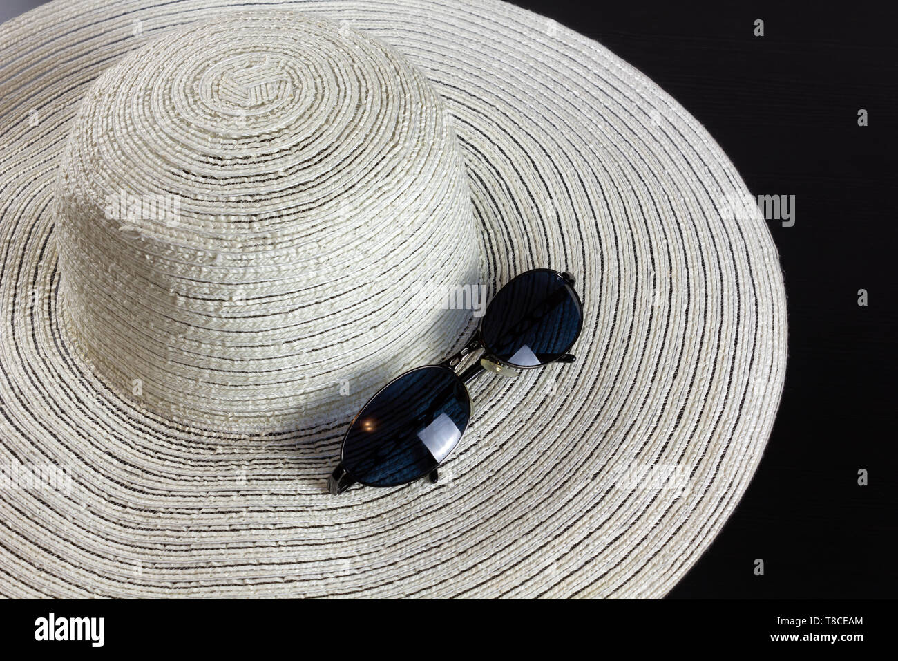 Weiße Stroh Hut auf einem dunklen Hintergrund, mit ein paar blaue schattierte Sonnenbrille Stockfoto