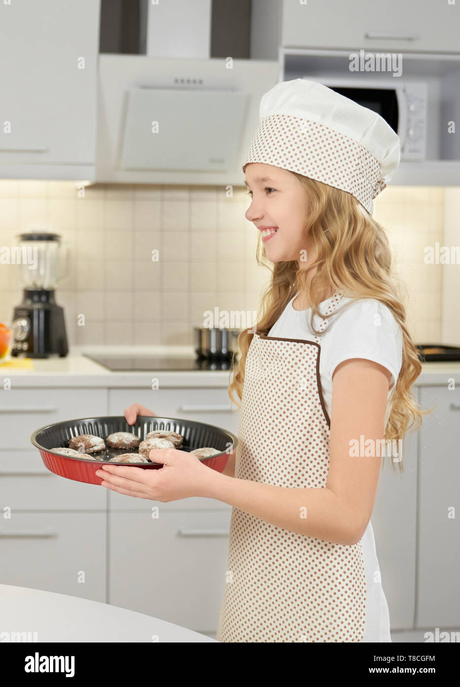 Charmantes, kleines Mädchen, dass Metall square backen Form mit hausgemachte Schokolade Cookies. Fröhlicher, lustiger Jugendlicher tragen in Chef hat und Schürze, lächelnd, entfernt. Stockfoto