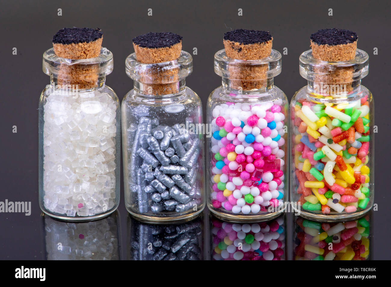 4 Glasflaschen mit bunten Süßigkeiten und Kuchen Dekoration gefüllt Stockfoto