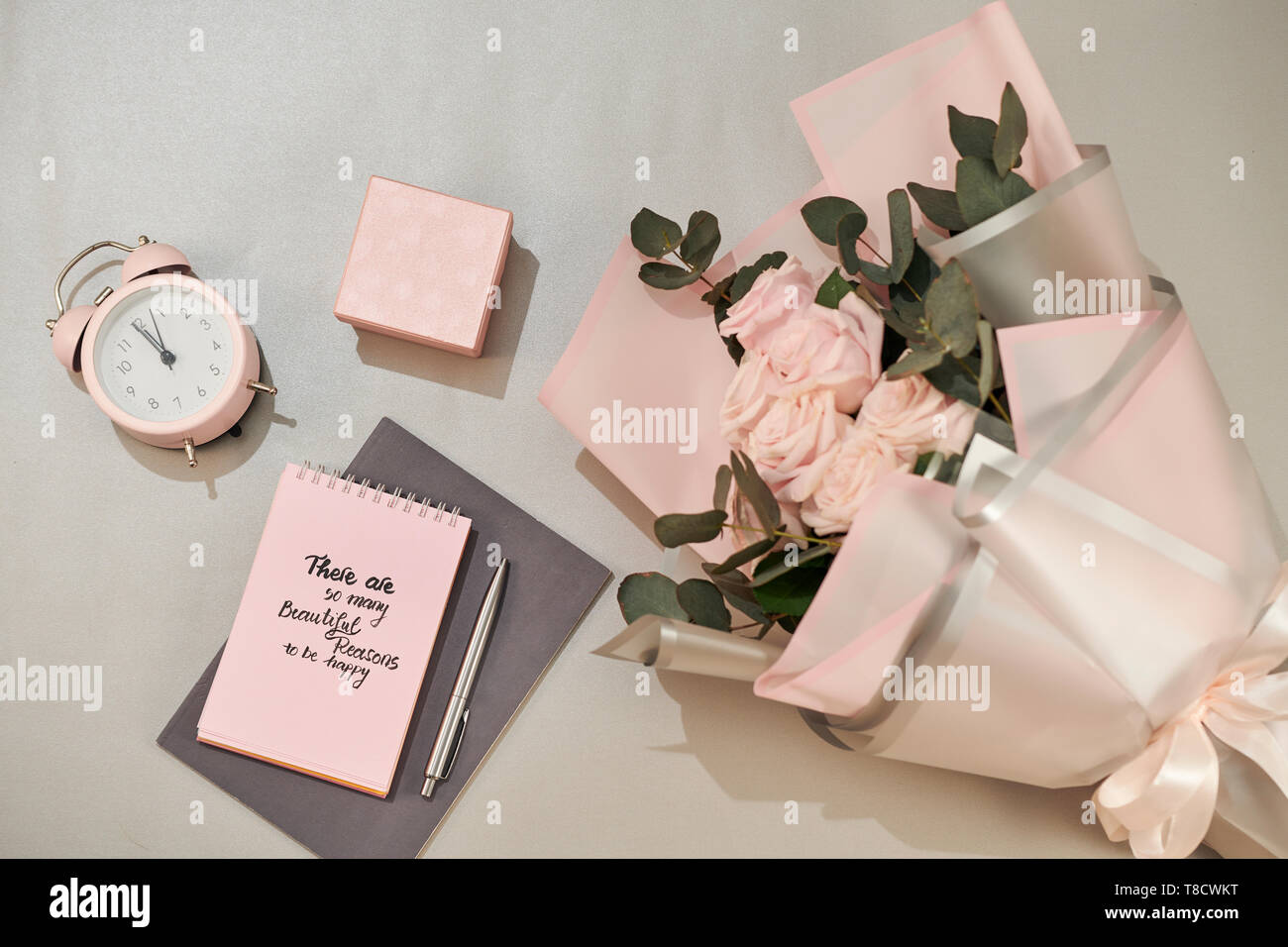 Geschenkbox, Wecker und rosa Rose Blüten am weißen Tisch Draufsicht in Flach Stil. Grußkarte für Mutter oder Frau Tag. Stockfoto