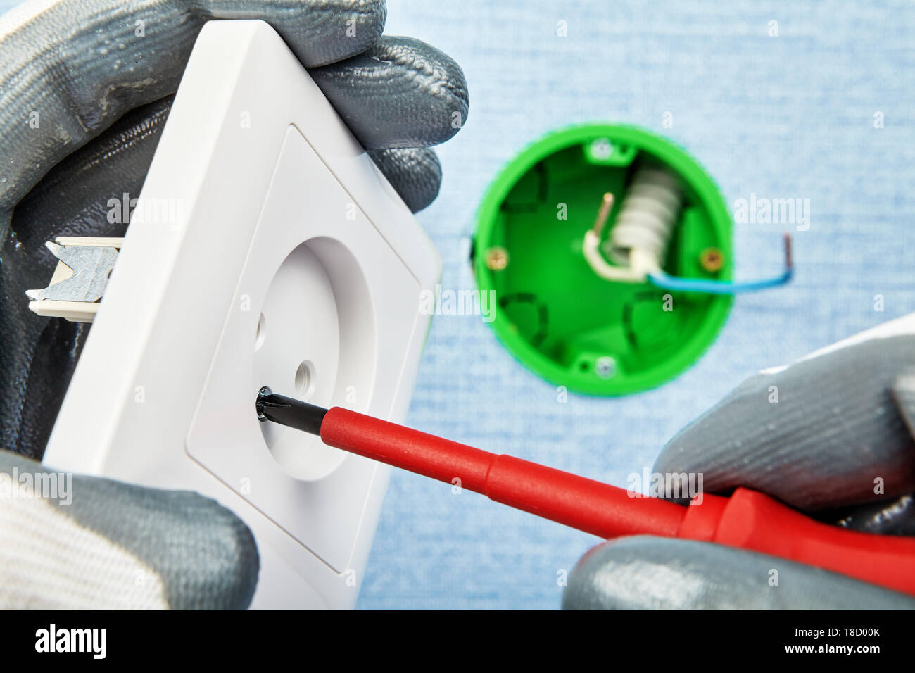 Elektriker in Schutzhandschuhe verdreht Schraube in neuen europäischen Standard Sockel mit Schraubendreher mit runden Anschlussdose auf dem Hintergrund. Stockfoto