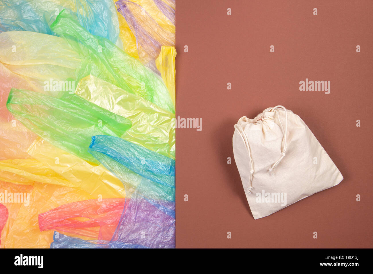 Viele bunte Plastiktüten mit einem eco-natürliche, wiederverwendbare Tasche zum Einkaufen auf braunem Hintergrund. Null Abfall, Umweltfreundlich, kein Plastik Konzept Stockfoto