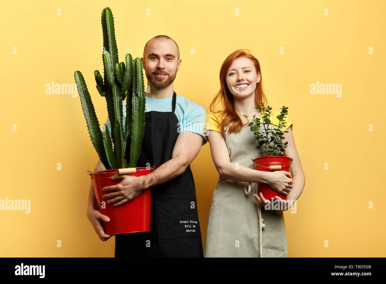 Gerne fröhliche junge Paar mit Blumen an die Kamera posieren. Isolierte gelben Hintergrund, studio Shot, Beruf, Hobby, Emotion, Gefühl Stockfoto