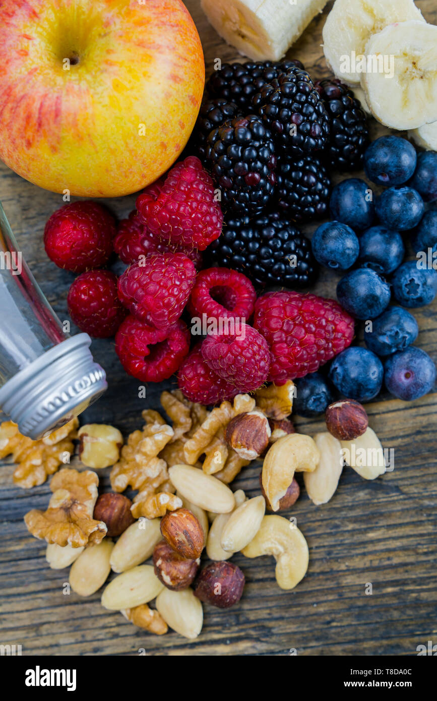 Horizontale Sicht auf eine Auswahl von Nüssen und Beeren und Bananen mit einer Flasche Quellwasser als gesunder Snack auf einem urigen braune Holztisch Stockfoto