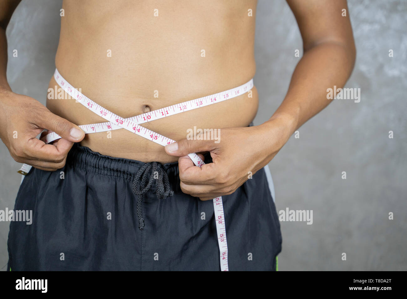 Übergewicht asiatischer Mann prüfen Sie überschüssiges Fett von Taille body mit Maßband. Fetter Mann mit großen Bauch. Ernährung und Gewicht zu verlieren. - Bild Stockfoto