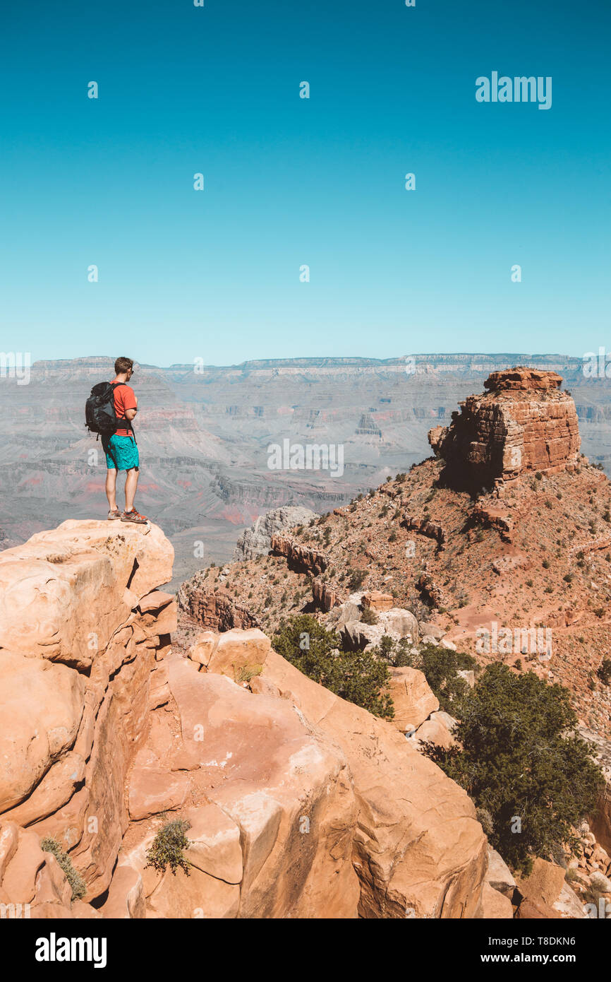 Ein junger männlicher Wanderer steht auf einem Felsen genießen Sie den herrlichen Blick auf den berühmten Grand Canyon mit dem Colorado River fließt an einem sonnigen Tag Stockfoto