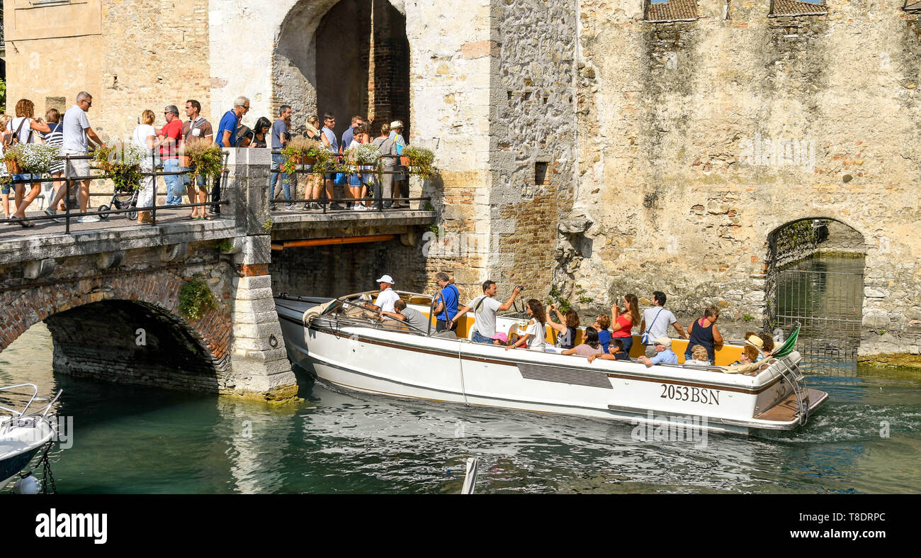 SIRMIONE, Gardasee, Italien - September 2018: Eine Stadtrundfahrt Motorboot voller Touristen vorbei unter die Leute auf der Brücke in die Scaliger Burg in der Stockfoto
