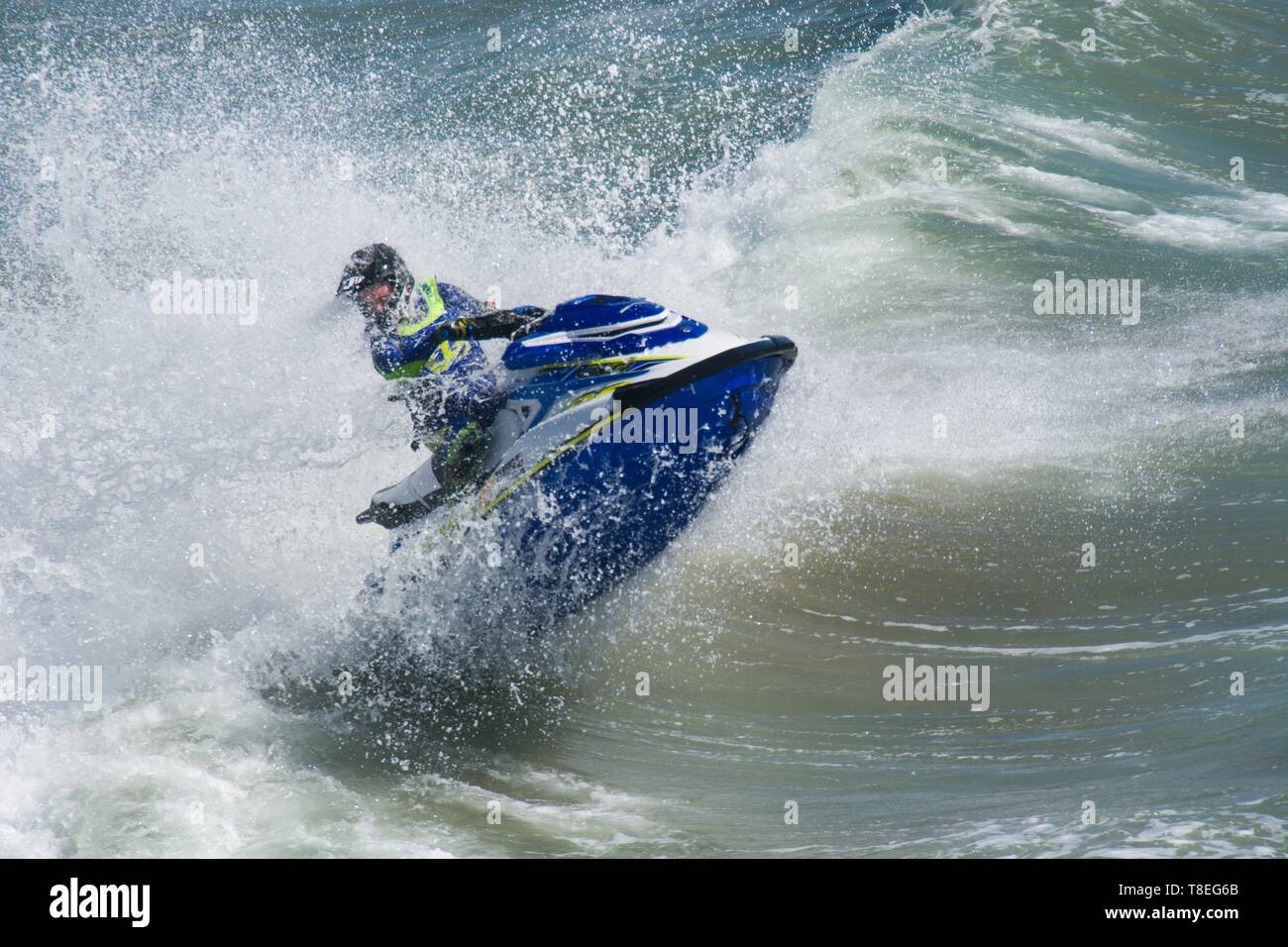 Huntington Beach, Kalifornien / USA - 7. April 2019: Jetskifahrer springt auf eine Meereswelle, wobei das Wasser beim Rennen dramatisch spritzt. Stockfoto