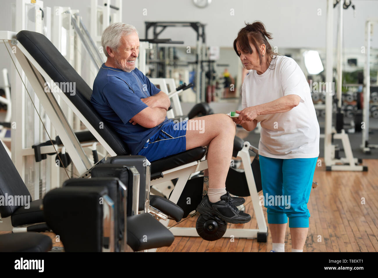 Ältere Menschen leiden unter Knieschmerzen nach wokout. Ältere Frau Anwendung der Salbe Creme auf verletzte mans Bein an der Turnhalle. Menschlichen Ausdruck von Schmerz. Stockfoto