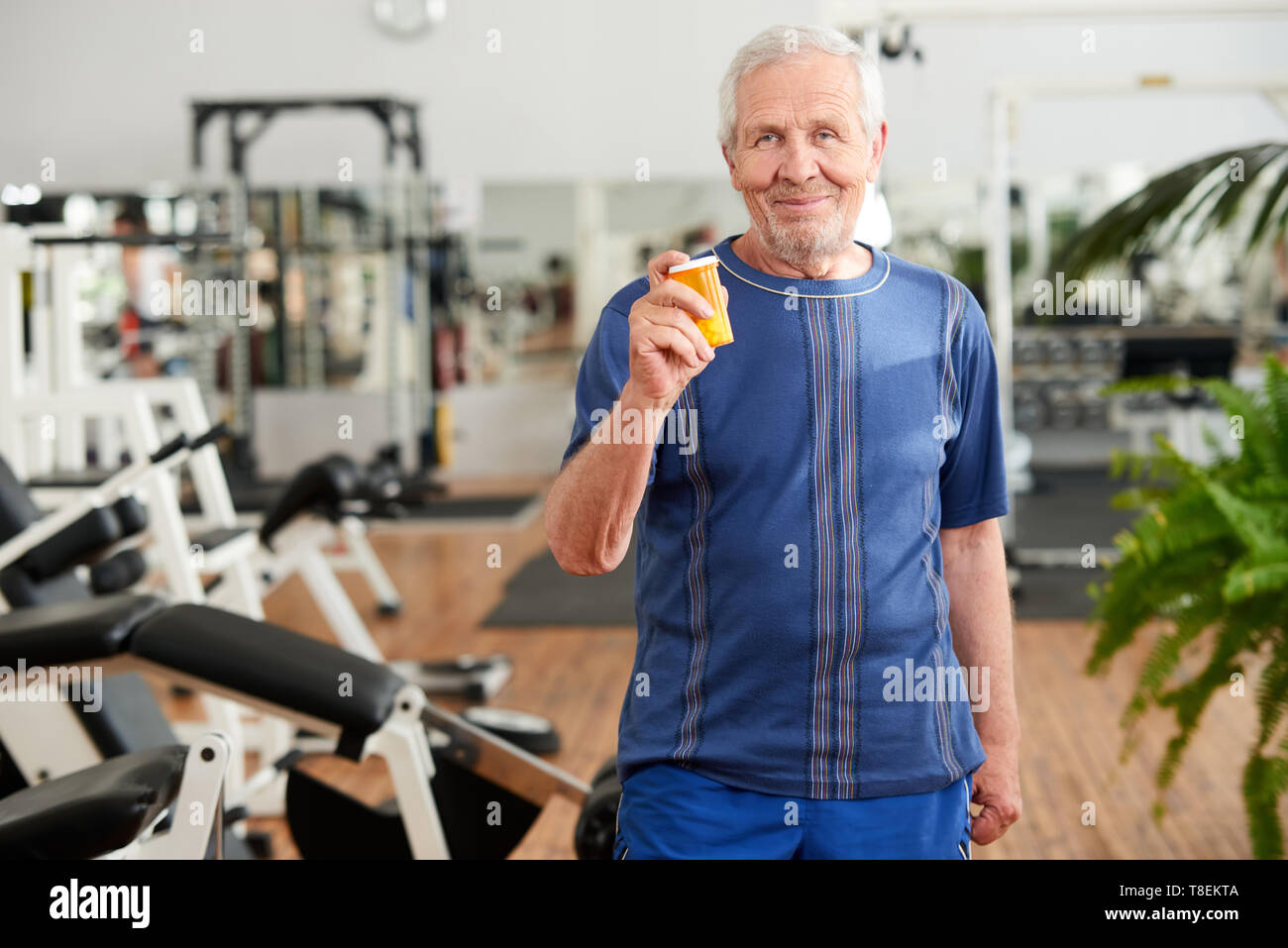 Älterer Mann mit Pillen im Fitnessstudio. Älterer Mann mit einer Flasche Ergänzung im Fitness Studio. Leute, Sport und Gesundheitswesen Konzept. Stockfoto