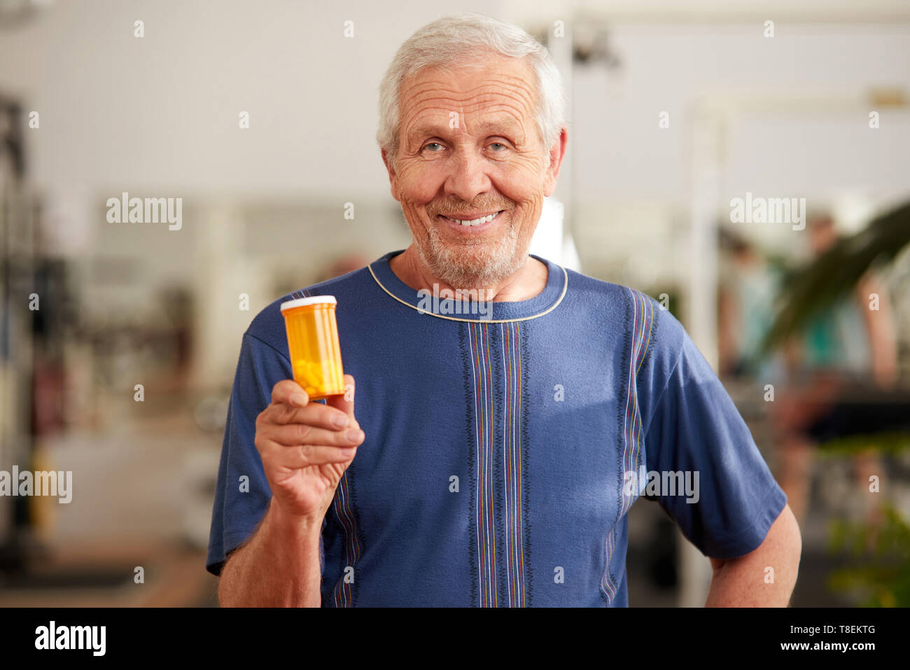 Lächelnd älterer Mann mit Flasche Pillen. Porträt der ältere Mann an der Kamera auf verschwommenen Hintergrund. Sport ergänzen das Konzept. Stockfoto