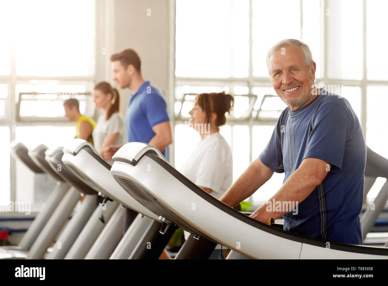 Lächelnd alter Mann trainieren im Fitnessstudio. Ältere Menschen in Sportkleidung auf Laufband und Kamera. Bleiben Sie aktiv durch ihre Jahre. Stockfoto